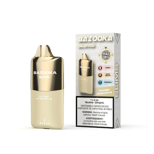 A Bazooka Slims disposable vape device in Mango Pineapple flavor stands next to its retail packaging box on a clean white background. The device features a metallic gold upper section and a light beige lower section, while the box displays the product name, flavor, and health warnings.